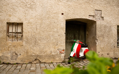 Vintage motorbike in italian flag colors parked near old rustic wall. Inspiring atmospheric spirit of Italy. Large textured foreground on left side of wall.