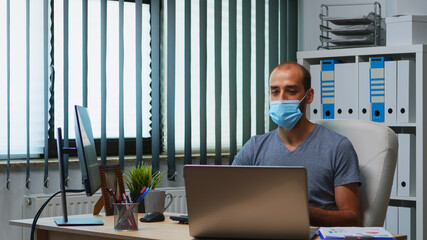 Man using laptop discussing project online wearing protective mask. Freelancer working in new normal office workplace chatting talking having virtual conference, meeting, using internet technology