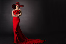 Woman Red Dress And Hat. Fashion Model In Long Evening Gown With Flowers. Black Studio Background.
