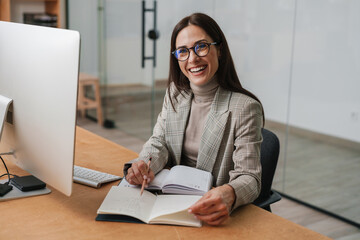 Wall Mural - Joyful charming woman in eyeglasses working with computer and planner