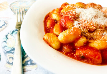 Portion of gnocchi in tomato sauce with grated parmesan cheese served in a white ceramic plate.