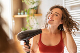 Happy smiling woman using hair dryer in bathroom