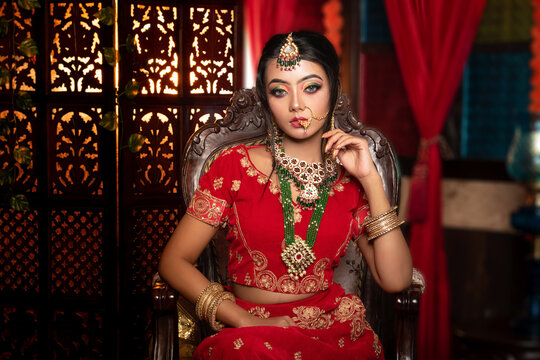 Magnificent young Indian bride in luxurious dress and precious jewellery is sitting in a chair in a luxury apartment. Classic vintage interior. Wedding fashion.