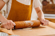 Hands of pastry woman rolling out dough with rolling pin on the table