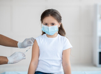 Poster - Little girl in face mask being vacciniated against covid-19 at hospital. Protection against contagious disease concept