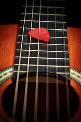 Wall Mural - Extreme closeup of a red guitar pick (plectrum) between the strings of the fretboard of an old acoustic guitar. String instrument.