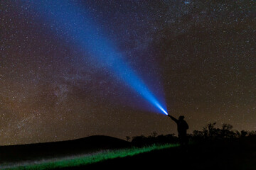 Wall Mural - Climber or backpacker. Light holds up over his head. Standing on mountain peak. man with flashlight point to the starry sky at midnight. tourist with flashlight