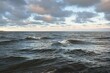 Panoramic view of the open Baltic sea at sunset. Dramatic sky with colorful glowing cumulus clouds. Water surface texture close-up. Fickle weather, winter, climate change, ocean swell, nature