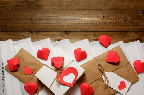 Valentine's day, love, romantic design from gifts and love letter with hearts, tied with twine with bows and labels, red paper hearts on white crepe paper and wooden planks background 