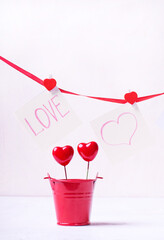 Valentine's Day composition on white. Red bucket with two decorative hearts and square stickers with the word 