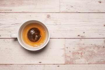 Partially filled and brewed cup of tea with a golden colour in a white mug on a textured white wooden table surface with copy space and room for text