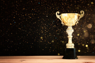 Wall Mural - image of gold trophy over wooden table and dark background, with abstract shiny lights