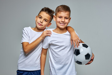 active boys with soccer ball in hands, young caucasian teenagers posing, hugging each other, engaged in sport, play in the same team