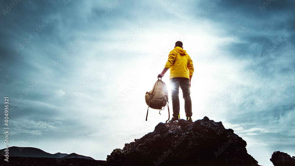 Young man with backpack standing on the top of a mountain at sunset - Goals and achievements - obrazy, fototapety, plakaty 