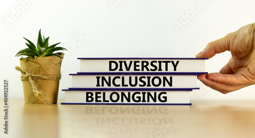 Diversity, inclusion and belonging symbol. Books with words \'diversity, inclusion and belonging\' on beautiful white background. Male hand,  plant. Diversity, business, inclusion and belonging concept.
