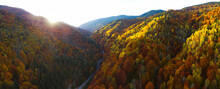 Aerial Drone Panorama Of Sun Setting Above The Forested Hills Of Lotru Mountains. Autumn Season, The Trees Are All Colored. Dusk Time - Only The Peaks Of The Crests Are Illuminated By The Sun Rays.