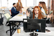 © Roman - woman celebrating personal achievement, sitting with computer in the office while colleagues are working in the background