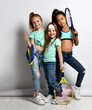 Happy sporty kids love exercise and a healthy lifestyle. Little girls in jeans, sports T-shirts with a water bottle, a big tennis racket, a fitness elastic band with thumbs up. Isolated studio shot