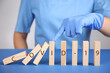 © New Africa - Doctor stopping domino effect at blue table, closeup. Prevent spreading of coronavirus