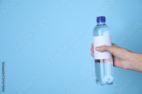 Obraz Dibond Woman holding plastic bottle with soda water on light blue background, closeup. Space for text
