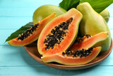 Fresh ripe papaya fruits with green leaves on turquoise wooden table, closeup
