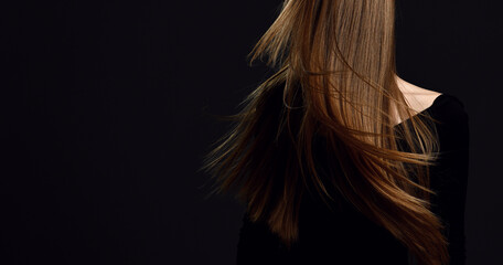 Portrait of woman shaking her head to makes her healthy strong long hair restored after spa procedures treatment flying over dark background with copy space . Hairstyle. Hair cosmetics