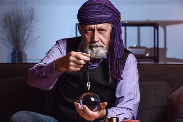 Wall Mural - Male fortune teller with crystal ball and pendulum at home