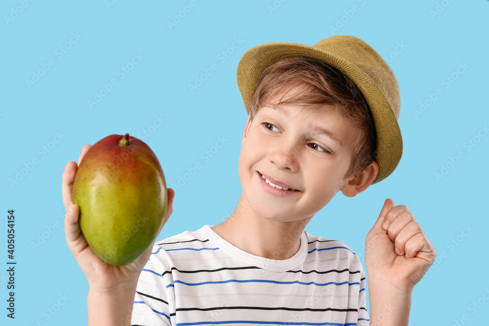 Cute little boy with fresh tasty mango on color background