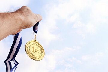 Wall Mural - man hand raised, holding gold medal against sky. award and victory concept
