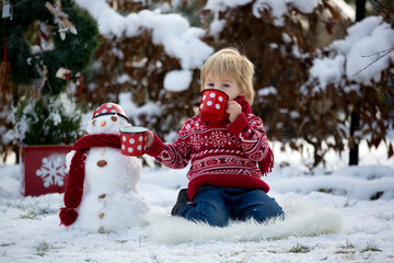 Wall Mural - Sweet blond toddler child, boy, playing in garden with snow, making snowman, happy kid winter time