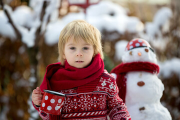 Canvas Print - Sweet blond toddler child, boy, playing in garden with snow, making snowman, happy kid winter time