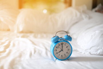 Blue vintage alarm clock on the bed at home with sunlight effect. Wake up energy. Soft morning time background concept. Selected focus.