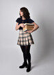 © faestock - full length portrait of pretty brunette woman wearing tartan skirt and boots.  Standing pose holding books against a  studio background.