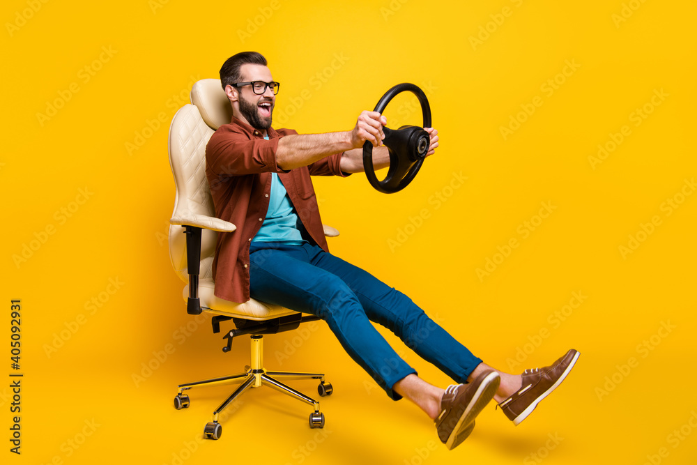 Full length body photo of playful crazy man in chair holding steering wheel pretending car rider isolated vivid yellow color background - obrazy, fototapety, plakaty 