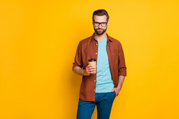 Poster - Photo portrait of bearded man in glasses keeping cup with coffee in casual clothes isolated on vivid yellow color background