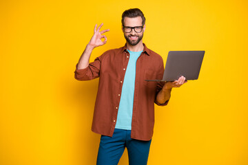 Photo of young handsome man gesture okey sign perfect good choose recommend promo laptop isolated over yellow color background