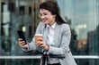 © Zoran Zeremski - Businesswoman with electric scooter standing in front of modern business building looking at phone.