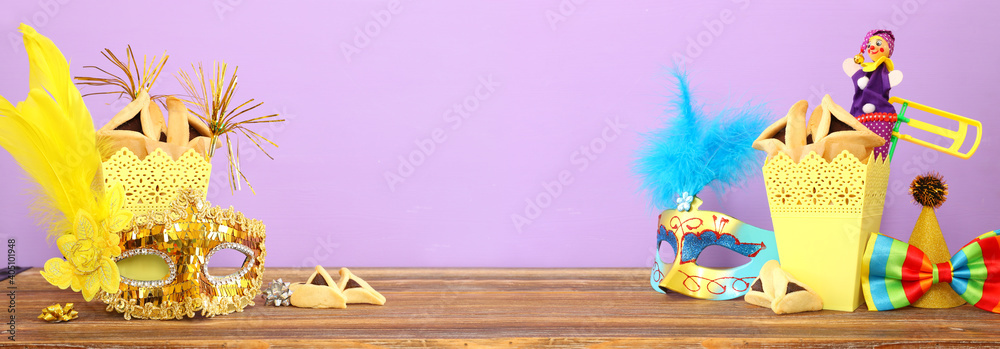 Purim celebration concept (jewish carnival holiday) over wooden table and purple background - obrazy, fototapety, plakaty 