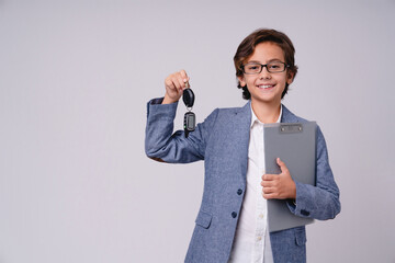 Wall Mural - Clever young boy future estate agent holding a clipboard and keys isolated over grey background