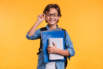 clever young boy holding folders for studing at school isolated over yellow background