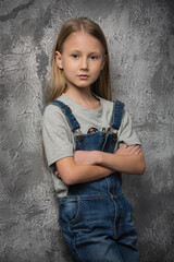 Canvas Print - girl child in a gray t-shirt and denim overalls on the background of an old wall