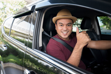 Young handsome asian man getting the new car.He driving car and showing thumbs up very happy. Buy or rent a car concept.