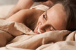 © monchak - beautiful girl basks in natural beige cotton bedding, she looks very happy and cozy