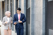 © NVB Stocker - Young business muslim woman and business man colleague walking and discussing outside the office. Woman is holding a coffee and businessman is holding a digital tablet outdoor.