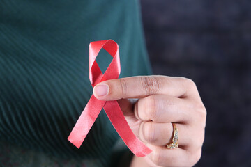 women hand holding red HIV ribbon isolated on black 