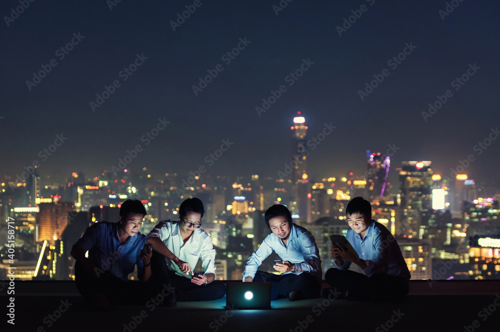 Smiling Businessmen Using Laptop While Sitting On Building Terrace At Night - obrazy, fototapety, plakaty 