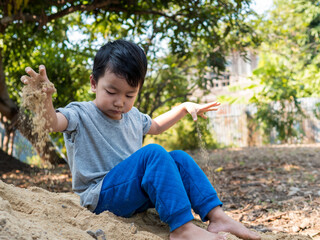 Asian child boy playing on sand outdoor with cute face in nature background. Happy kid enjoy in relaxing day, preschool learning ef, family activity in summer, freedom concept.