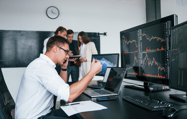 Man uses laptop. Team of stockbrokers works in modern office with many display screens