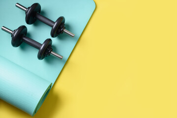 Wall Mural - Sport black dumbbells on turquoise yoga mat on yellow background. Copy space. Flat lay. View from above.