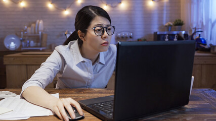 Wall Mural - tired frowning woman worker in glasses working late at night at home kitchen. office lady sitting at desk and connecting to internet on laptop computer in evening. exhausted female staring at screen